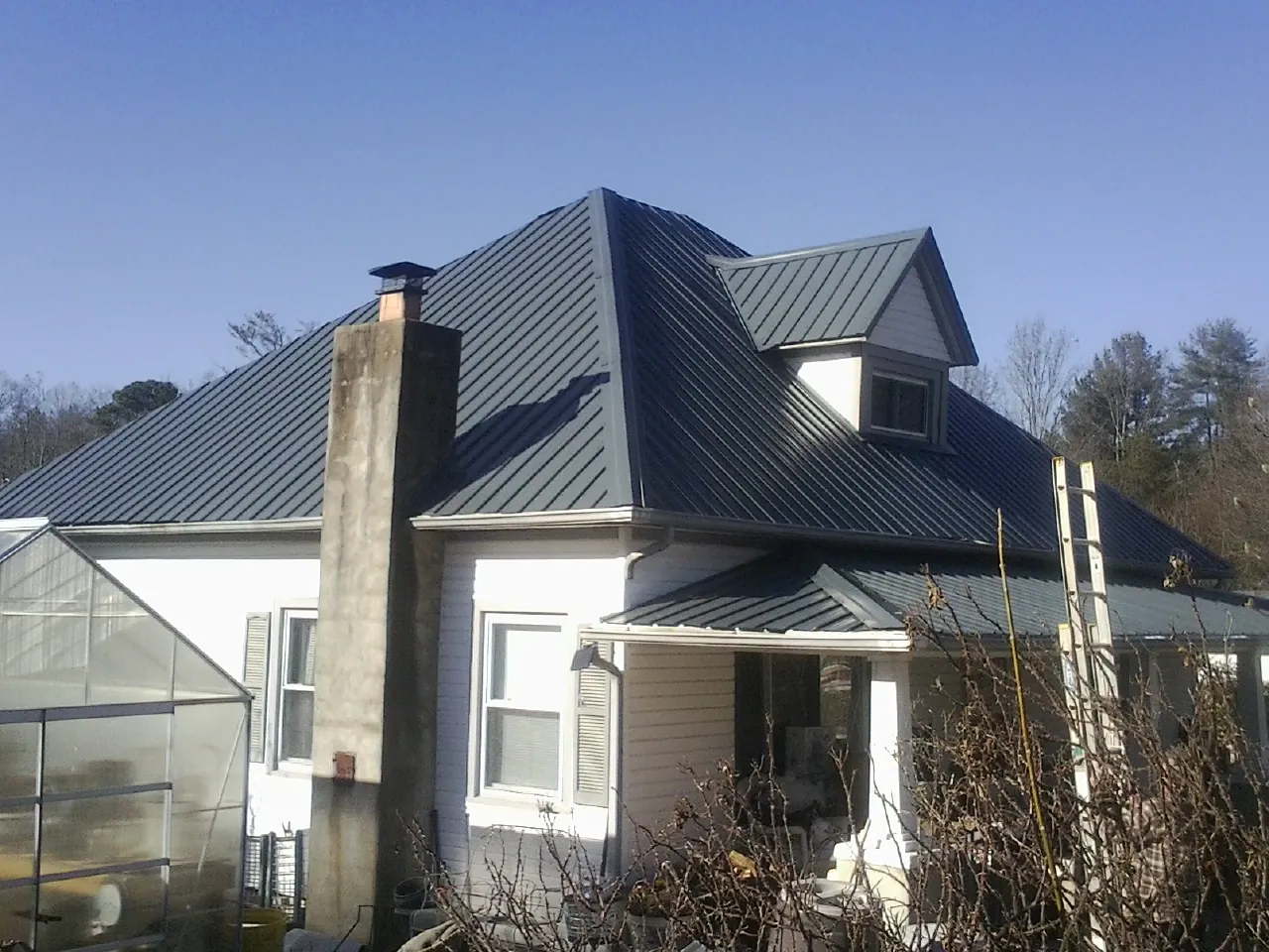 Dark blue standing seam metal roof on a white farmhouse with dormer — Slate & Tile Roof Repair by Roofing Brothers in Prattville