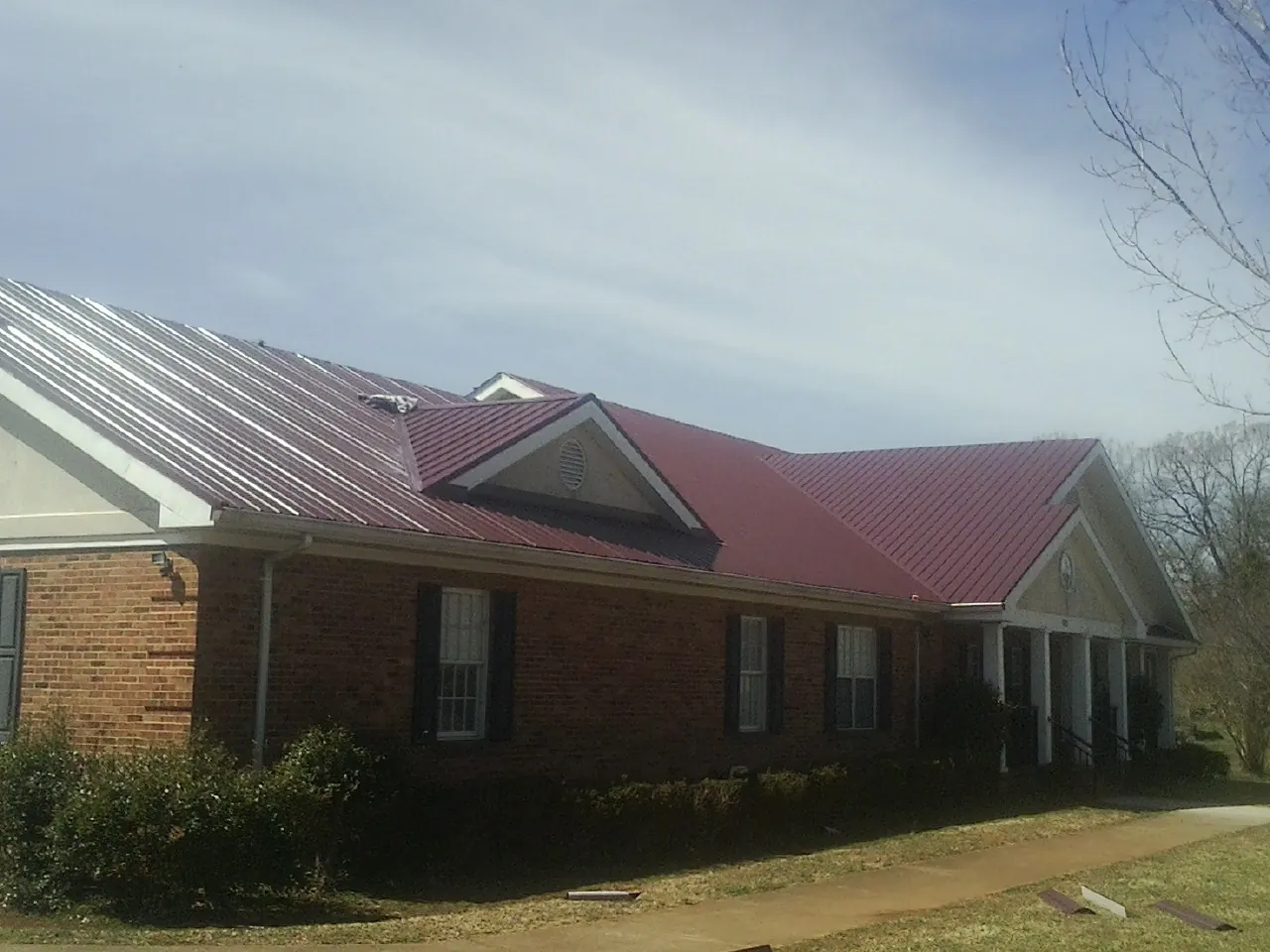 Red metal roof with gabled entries on a long brick building, from a Hail Damage Roof Repair job in Prattville