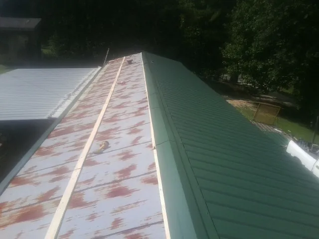 Old rusted panels beside newly installed green metal roofing — Wind Damage Roof Repair by Roofing Brothers in Prattville