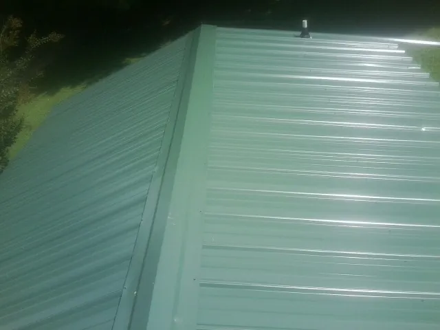New green metal panels meeting at the ridge of a roof — Flat Roof Repair work by our crew in Prattville