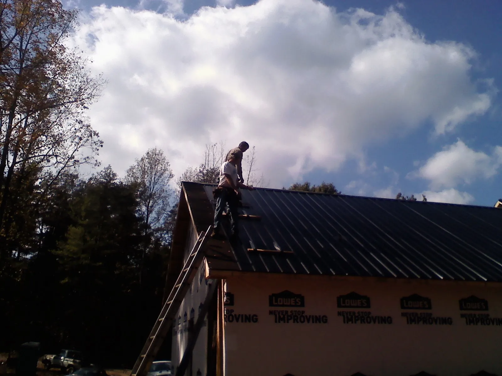 Roofer fastening dark metal panels high against a cloudy sky, from a Roof Inspection job in Prattville