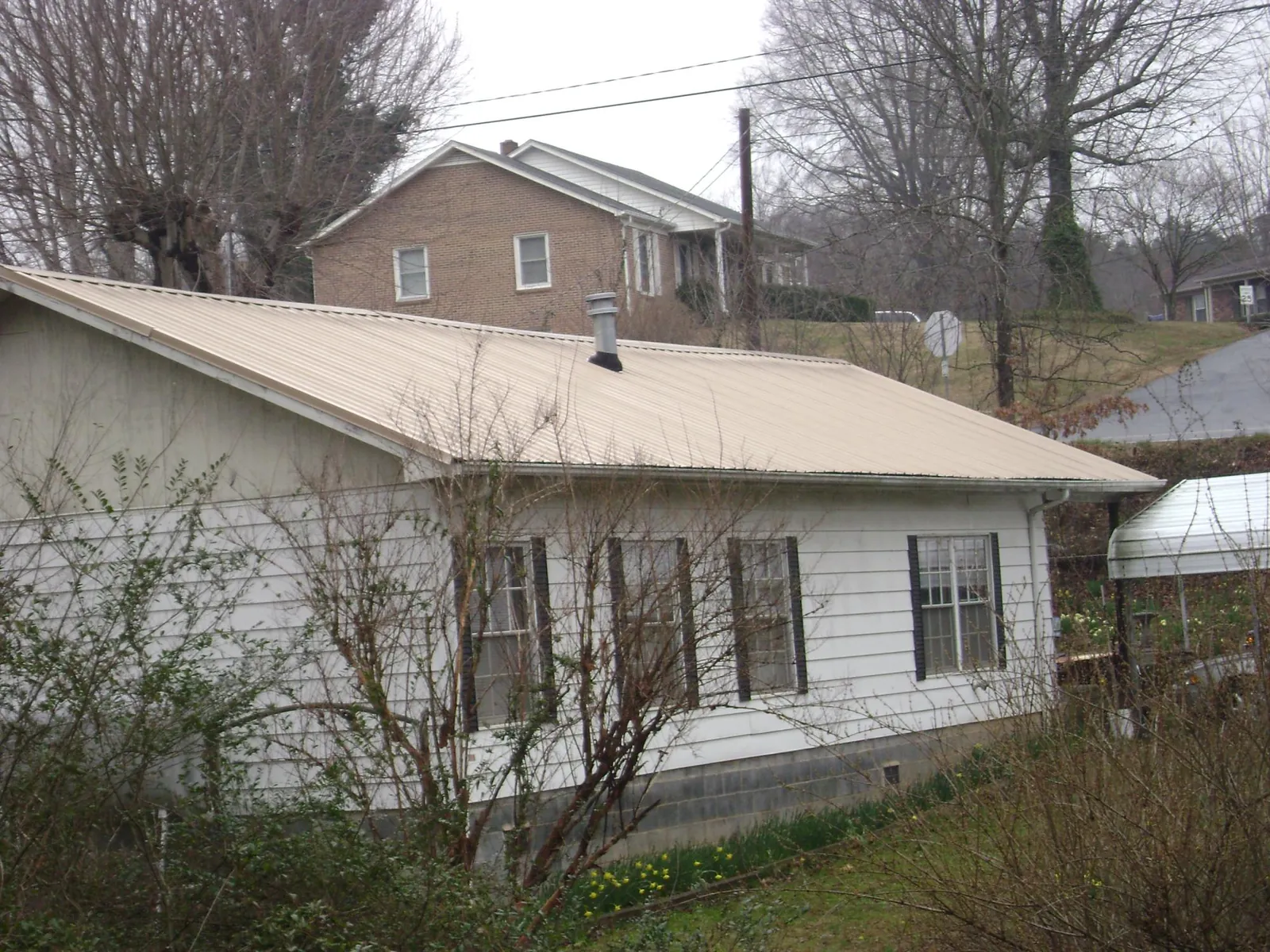 Tan metal roof on a white sided house set into a hillside — Commercial Roofing by Roofing Brothers in Prattville
